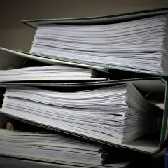 Stos grubych segregatorów z dokumentami, każdy z nich czynny zal.