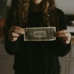 Dłoń trzyma banknot jednodolarowy, symbolizujący początek budowania majątku.