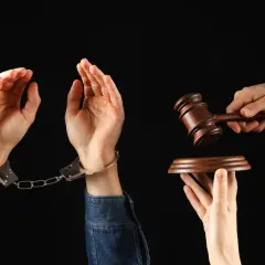 Ręce w kajdankach, młotek sędziowski i deska. Symbol naruszenia dóbr osobistych i sprawiedliwości.