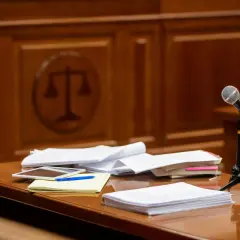 Stół w sali sądowej z dokumentami, mikrofonem i symbolem sprawiedliwości w tle. Czas na rozprawę sądową.