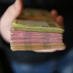 Gruba paczka banknotów, różowych i żółtych, trzymana w dłoni. To zabezpieczenie finansowe, które daje poczucie bezpieczeństwa.