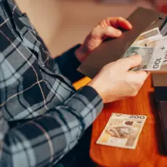 Osoba w kratę liczy pieniądze, przygotowując donos do urzędu skarbowego. Obok leży laptop i banknot 200 zł.