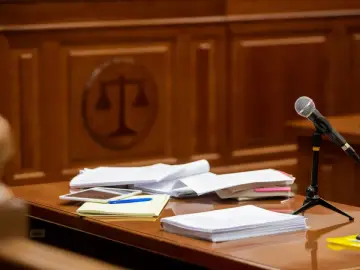 Stół w sali sądowej z dokumentami, mikrofonem i symbolem sprawiedliwości w tle. Czas na rozprawę sądową.