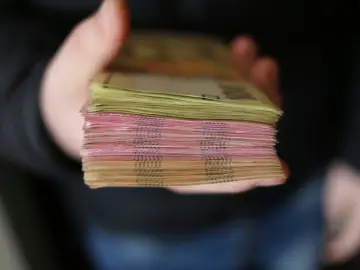 Gruba paczka banknotów, różowych i żółtych, trzymana w dłoni. To zabezpieczenie finansowe, które daje poczucie bezpieczeństwa.