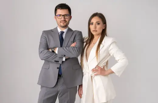 Para prawników w eleganckich strojach, mężczyzna w szarym garniturze, kobieta w białej marynarce.