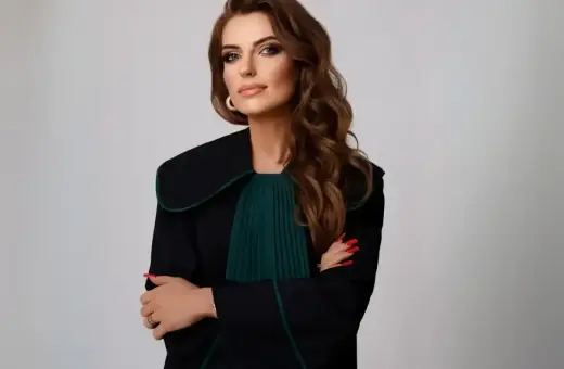 Kobieta w todze prawniczej, z rękami skrzyżowanymi na piersi, na jasnym tle.